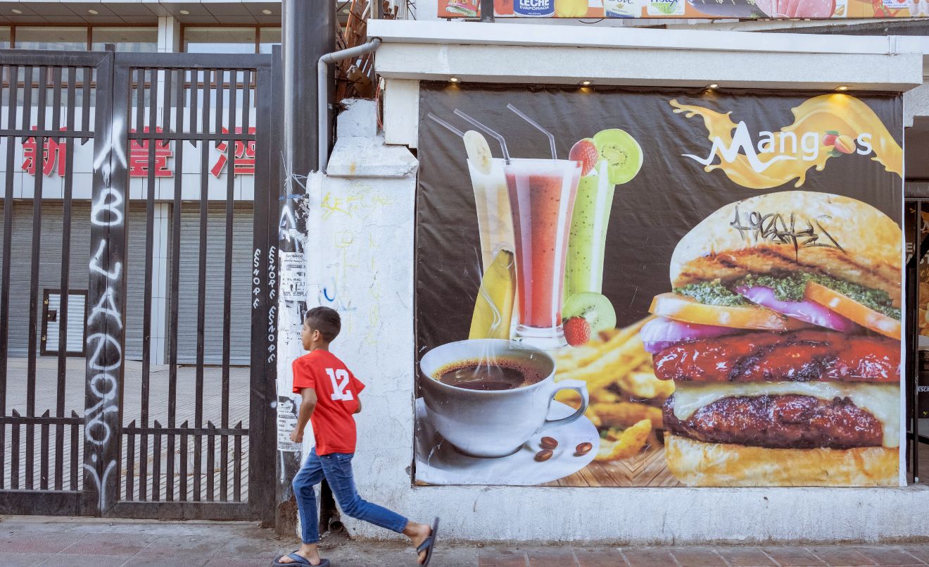 Un nen corre davant d’un cartell de menjar ràpid camí cap a una botiga de llaminadures, al centre de Santiago, Xile (UNICEF/UN0805425/Goupil)