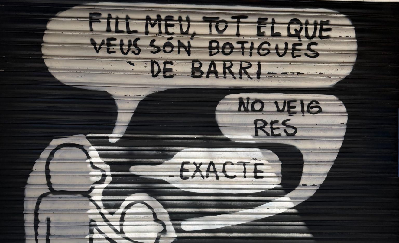 La persiana metàl·lica de la botiga Dulcidante amb un grafit d'un iceberg que diu “Les famílies que viuen de la botiga” (foto pròpia).